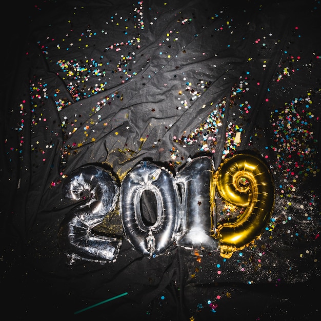 Free Photo 2019 balloons on dark fabric with confetti