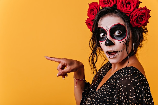 Ã¢ÂÂlose-up portrait of surprised girl pointing finger to left. Shocked woman in halloween image posing on isolated wall