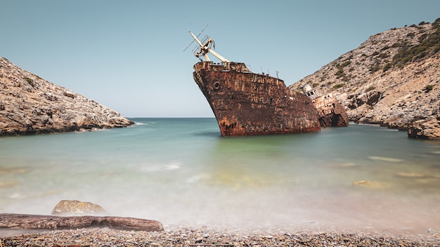 Abandoned rusty ship in the sea near huge rock formations under the clear sky