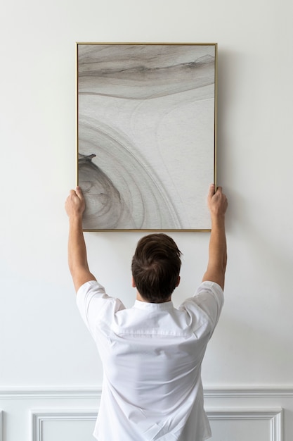 Free photo abstract painting being hung by a young man on a white minimal wall