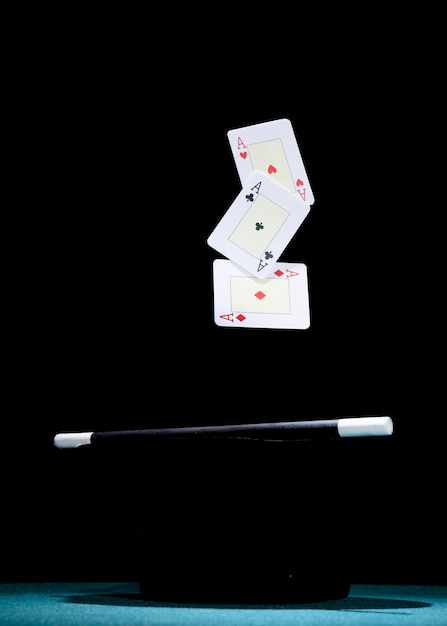 Free photo aces plying card over the black top hat and magic wand against black background