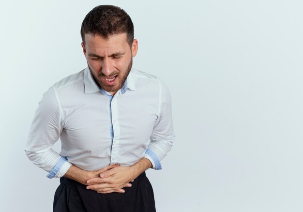 Aching handsome man holds belly with two hands isolated on white wall