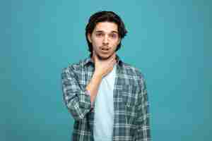 Free photo aching young handsome man looking at camera while keeping hand on neck having sore throat isolated on blue background