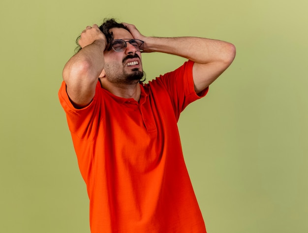 Free photo aching young ill man wearing glasses holding head suffering from headache with closed eyes isolated on olive green wall