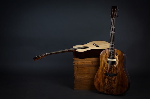 Acoustic guitar on a chair and close-up brown guitar in black wall.