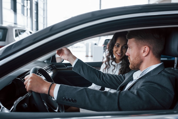 Active conversation. Lovely successful couple trying new car in the automobile salon