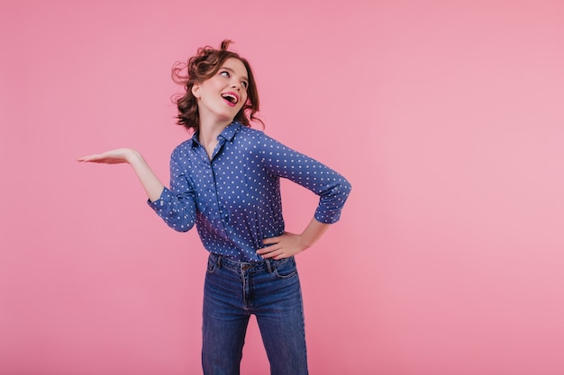 Active dark-haired girl in blue blouse dancing  Indoor photo of blithesome young lady with wavy hair having fun on pink wall.