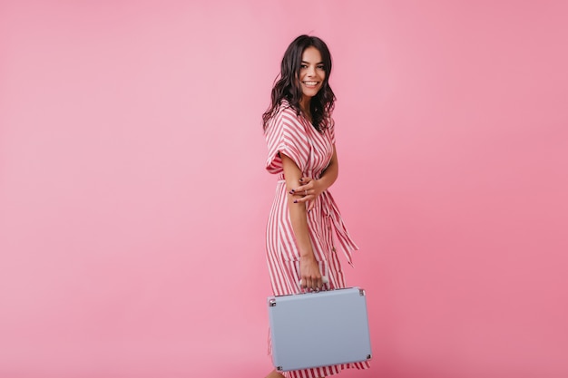 Free Photo active and positive brunette goes to airport with hand luggage. portrait of tanned girl in striped sundress.