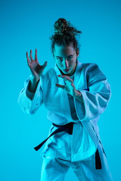 Active training. Professional female judoist in white judo kimono practicing and training isolated on blue neoned studio background.