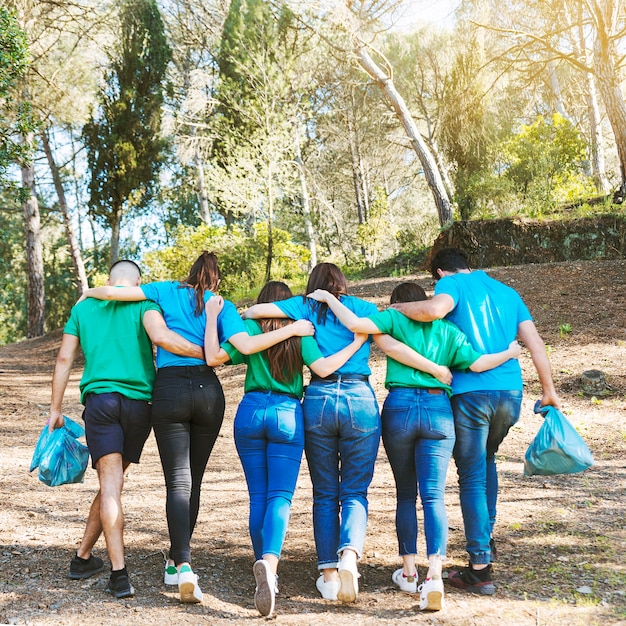 Free photo activists hugging walking with trash bags in woods