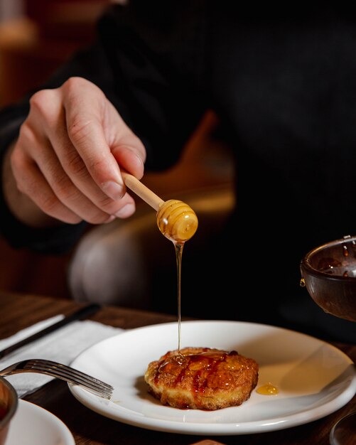 Adding honey to pancake inside white plate.