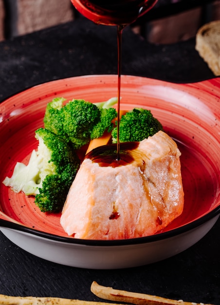 Free Photo adding teriyaki sauce to salmon steak with broccoli in pink bowl.