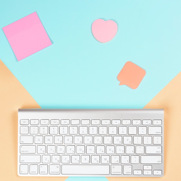 Free photo adhesive notepad; heart shape and speech bubble with wireless white keyboard on dual background