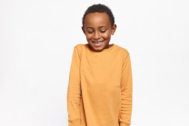 Free Photo adorable afro american kid in yellow sweater looking down shyly having timid facial expression