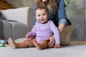 Free photo adorable baby being held by his mother and sitting on the floor