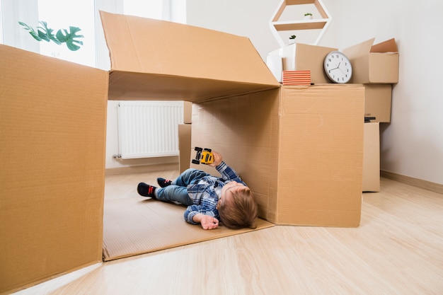 Adorable baby boy lying in the cardboard box playing with toy car at home