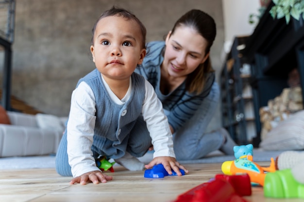 Adorable baby crawling on the floor and being helped by his mother