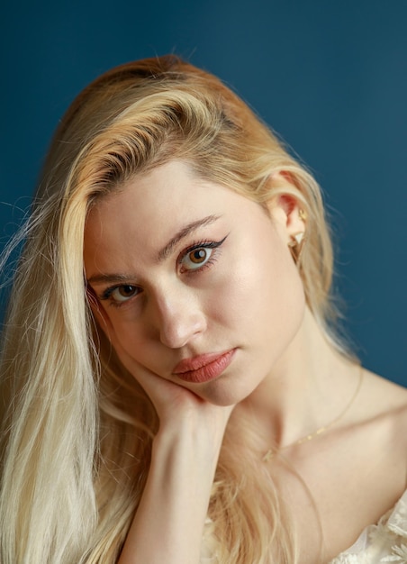 Free photo adorable blonde put her hand to her chin and looking at the camera on blue background