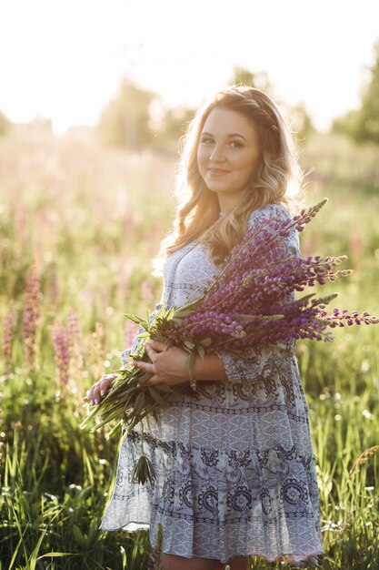 Adorable blonde woman in blue dress walks across the field of violet lavender flowers