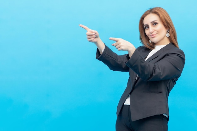 Adorable businesswoman standing on blue background and point her fingers aside