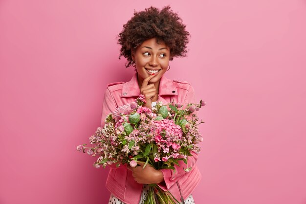 Adorable cheerful woman looks aside, gets bouquet of flowers, looks happily aside, poses