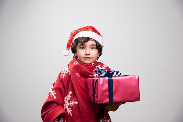 Adorable child in Santa hat holding Christmas gift