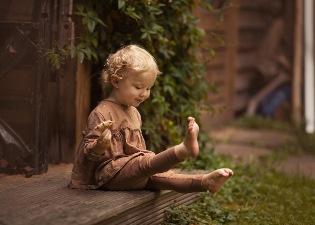 Adorable child sitting barefoot on the porch while eating a cookie