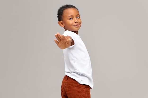 Adorable cute dark-skinned boy reaching out hand  making stop gesture or saying Goodbye. Handsome Afro American male child gesturing, giving sign, sending message. Nonverbal communication