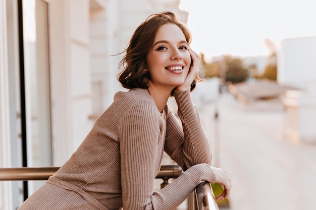 Adorable dark-eyed girl laughing at balcony. Photo of cheerful caucasian woman with beautiful smile.