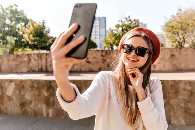 Free Photo adorable european woman in black sunglasses chilling in good autumn day outdoor shot of glamorous french grl making selfie on the street