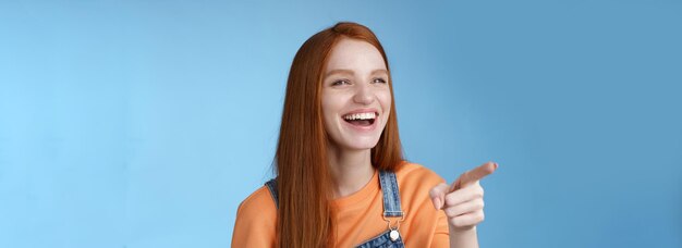 Adorable fascinated young attractive tender redhead amused girl having fun pointing looking left