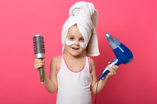 Adorable female child holding hair dryer and comb in hands