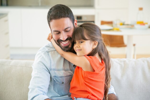 Adorable girl hugging her dad while sitting on his lap.