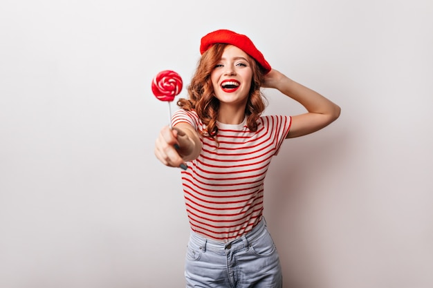 Adorable girl in red beret eating candy.  amazing french lady with ginger hair posing with lollipop.