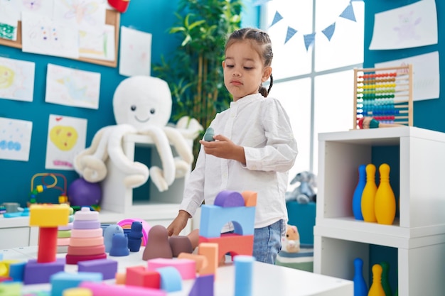 Free photo adorable hispanic boy playing with construction blocks standing at kindergarten