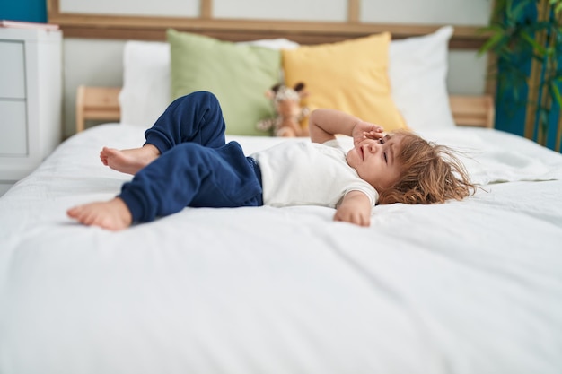 Adorable hispanic toddler lying on bed crying at bedroom