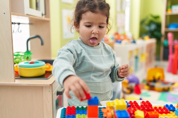 Free photo adorable hispanic toddler playing with construction blocks standing at kindergarten