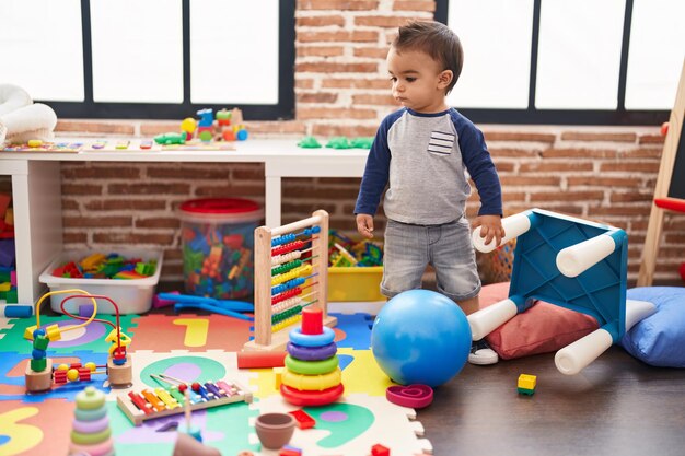 Adorable hispanic toddler standing with serious expression at kindergarten