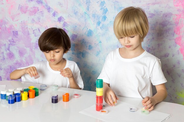 Adorable kids in white t-shirts playing with multicolored paints