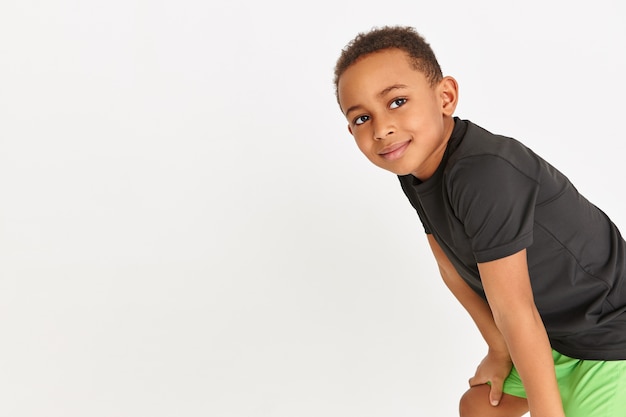 Free photo adorable little boy in black t-shirt and green shorts resting during cardio workout keeping hands above his knees