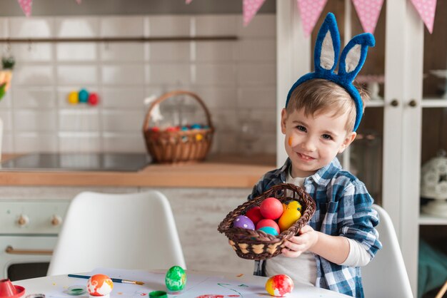 Adorable little boy with bunny ears holding a basket with eggs