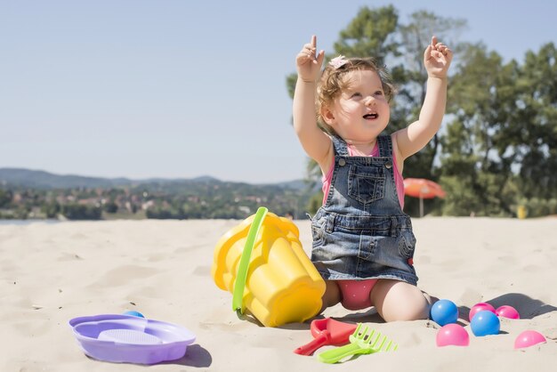 Adorable little girl playing on the beach with colorful balls and plastic toys