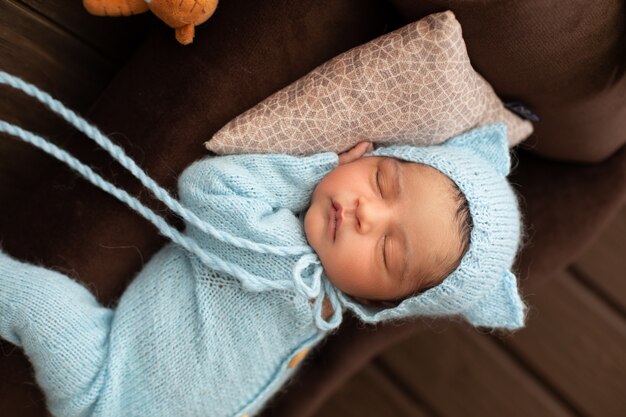 Adorable newborn pretty and likeable baby boy sleeping on brown sofa and pillow in blue crocheted pijamas