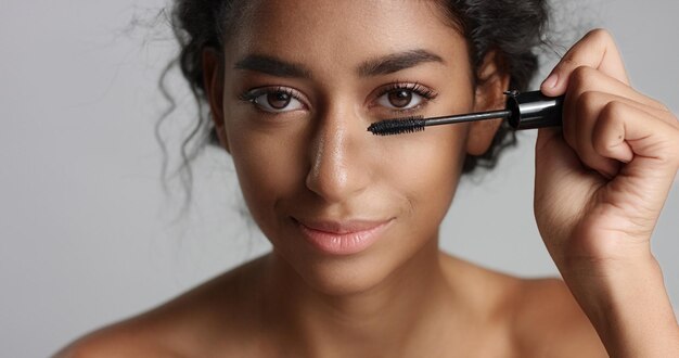 Adorable teenage Middle Eastern girl with great skin applying mascara to her long lashes on white background