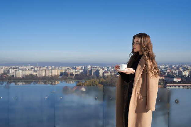 Adorable woman standing on balcony with cup of coffee