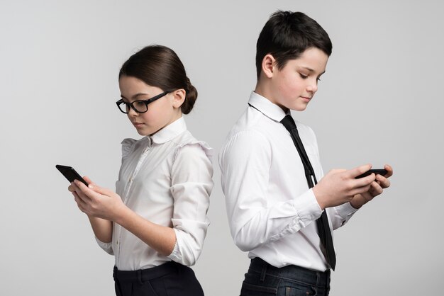 Adorable young boy and girl texting on mobile phones