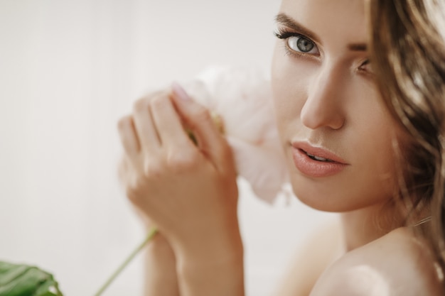 Free photo adorable young woman holds white flower before her face