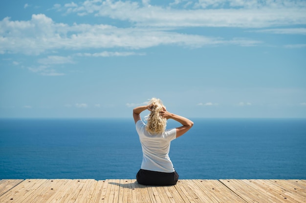 Free photo adult beautiful woman rejoices in a warm day blonde sits against the backdrop of a magnificent seascape a journey through the greek islands a famous place for vacation and travel