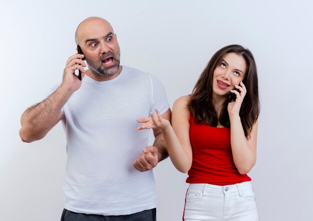 Adult couple both talking on phone impressed man looking at side and clueless woman looking up 