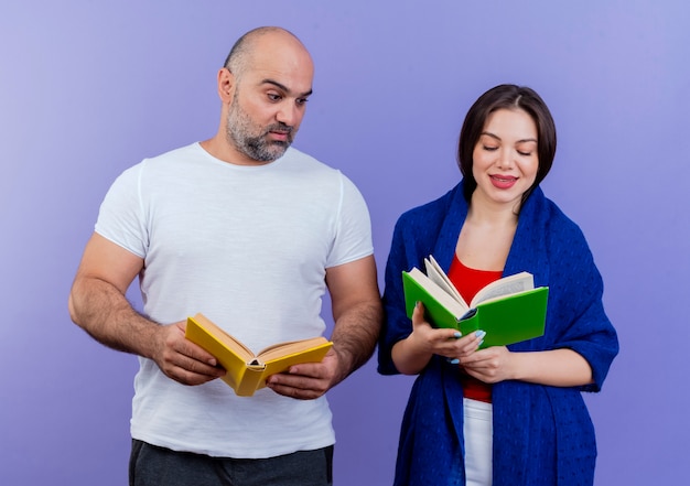 Free photo adult couple pleased woman wrapped in shawl reading book impressed man holding book and looking at her book